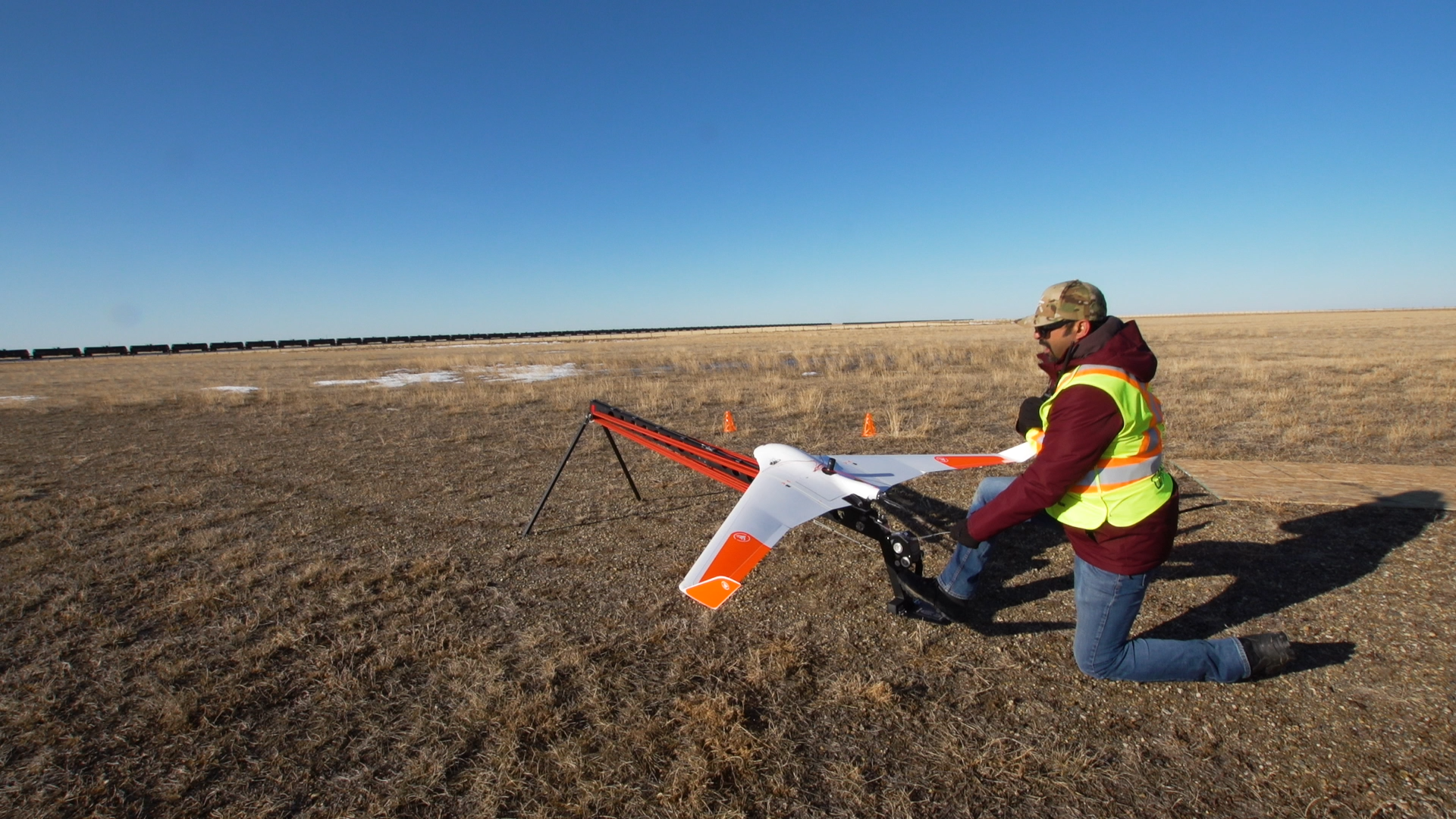 A person in a safety vest kneels outside as they set up an unmanned aircraft (drone)